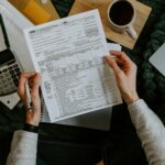 Hands holding tax forms with a calculator and laptop, representing Texas franchise tax filing